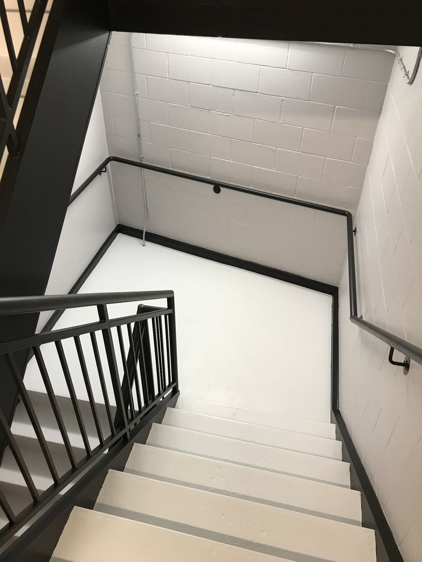 Condo stairwell after professional painting with clean white walls and black railings